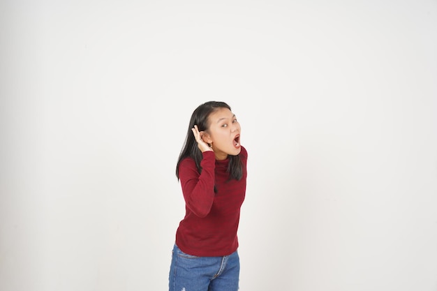 Mujer joven asiática en camiseta roja mano en la oreja no puede oírte concepto aislado en fondo blanco