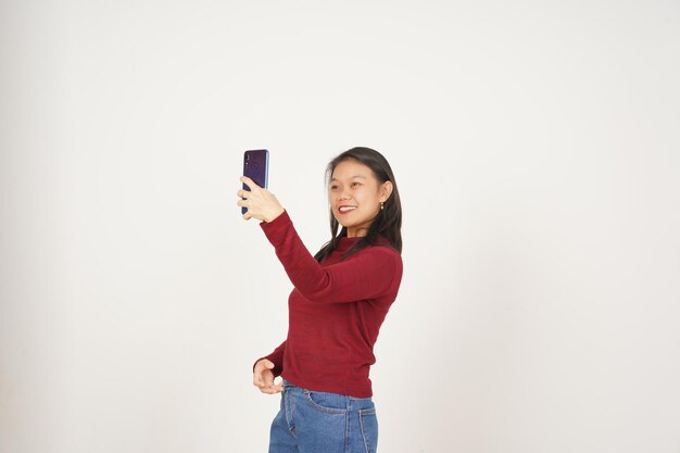 Foto mujer joven asiática con camiseta roja toma una foto de selfie aislada sobre un fondo blanco