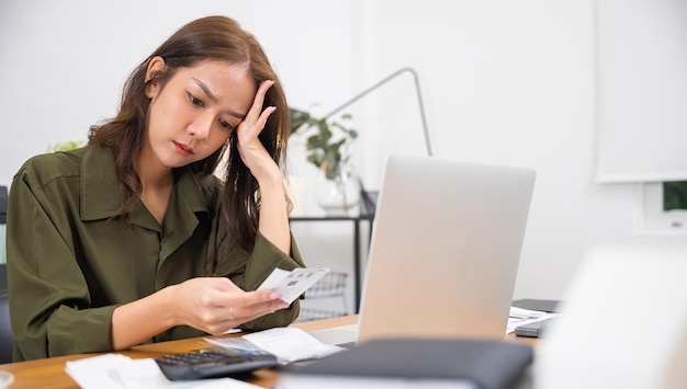 Mujer joven asiática con una computadora portátil con papeles en las manos que calcula el presupuesto financiero en el escritorio