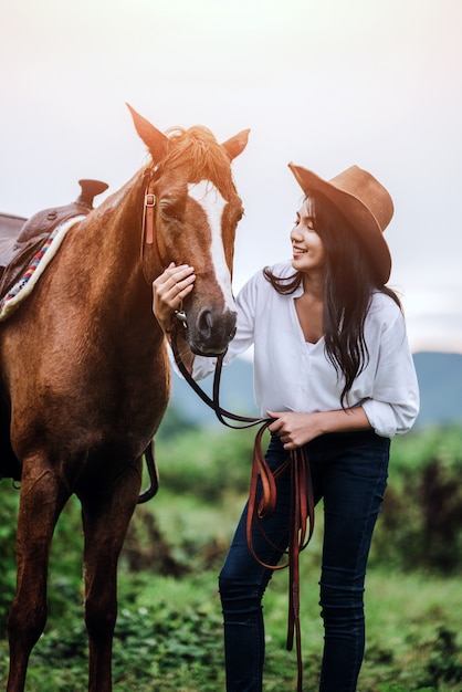 La mujer joven asiática cuida de su caballo de los soplos en la puesta del sol.