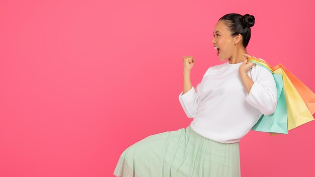 Mujer joven asiática emocionada con bolsas de compras celebrando el éxito