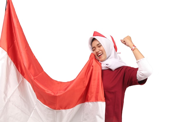 Mujer joven asiática encapuchada con camisa blanca besando la bandera roja y blanca de Indonesia en el fondo blanco