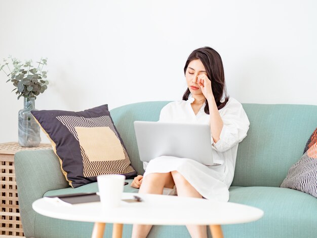 Mujer joven asiática frotándose los ojos cansados cuando usa la computadora portátil.