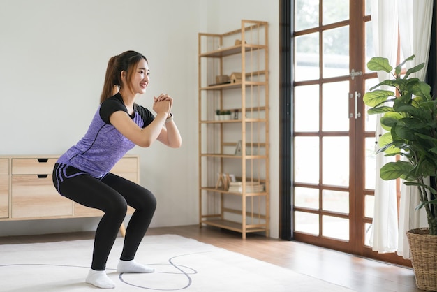 Mujer joven asiática haciendo ejercicio con ejercicios en cuclillas en el suelo para un estilo de vida saludable en casa