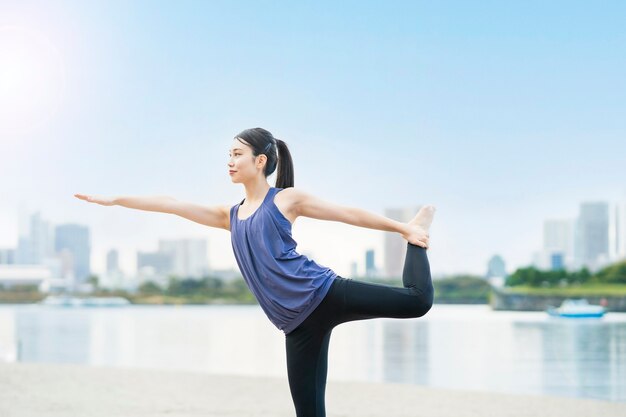 Mujer joven asiática haciendo yoga en la playa de la ciudad