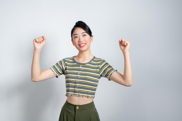 Mujer joven asiática levantando los brazos mientras sonríe y grita para celebrar después de un trabajo exitoso