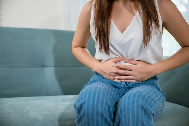 Mujer joven asiática manos infelices sosteniendo el estómago que sufre de dolor abdominal