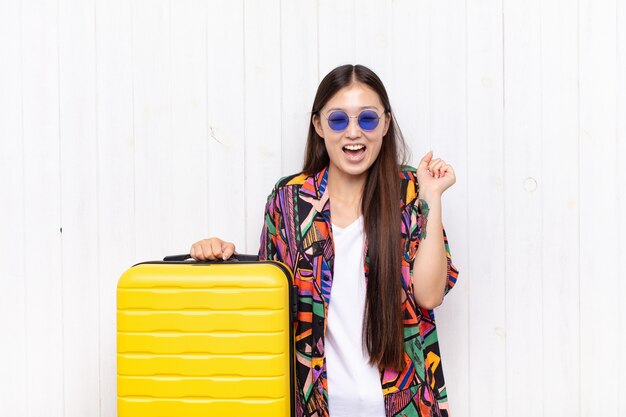 Mujer joven asiática que parece extremadamente feliz y sorprendida, celebrando el éxito, gritando y saltando. concepto de vacaciones