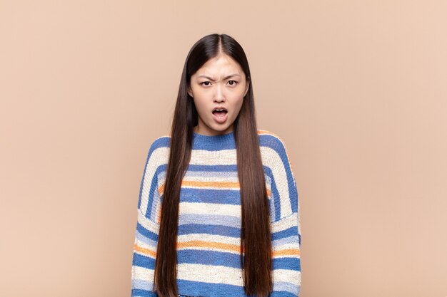 Mujer joven asiática que parece sorprendida, enojada, molesta o decepcionada, con la boca abierta y furiosa