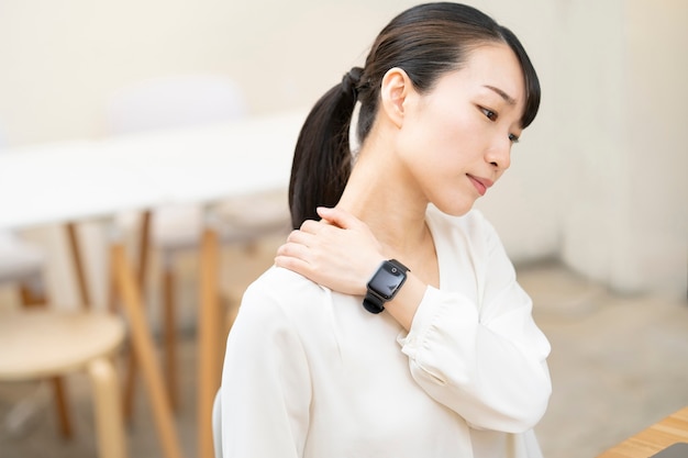Mujer joven asiática que se preocupa por la rigidez de los hombros durante el trabajo