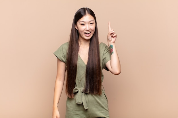 Mujer joven asiática que se siente como un genio feliz y emocionado después de realizar una idea, levantando alegremente el dedo, ¡eureka!
