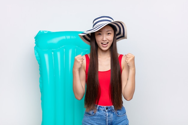 Mujer joven asiática que se siente sorprendida, emocionada y feliz, riendo y celebrando el éxito, diciendo ¡guau !. concepto de verano