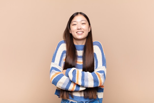 Mujer joven asiática riendo felizmente con los brazos cruzados, con una pose relajada, positiva y satisfecha