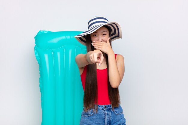 Foto mujer joven asiática riéndose de ti, apuntando aislado