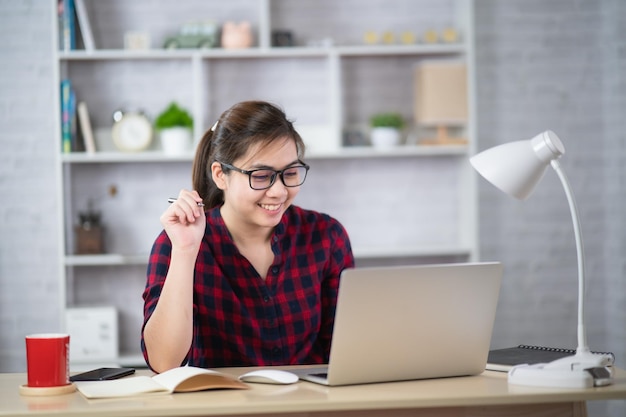 Mujer joven asiática en ropa elegante camisa blanca trabajando en la computadora portátil mientras está sentado en la oficina creativa o ca