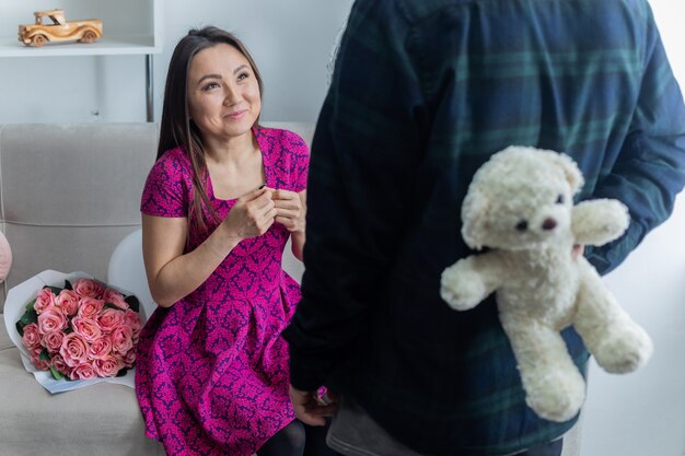 Foto mujer joven asiática sentada en un sofá con ramo de flores feliz y emocionado mientras recibe un oso de peluche como regalo