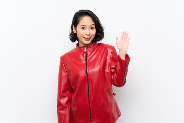 Mujer joven asiática sobre saludar blanco aislado con la mano con la expresión feliz