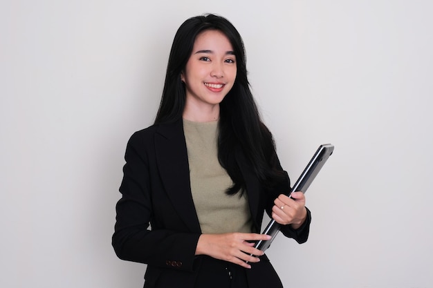 Mujer joven asiática sonriendo confiada mientras sostiene una computadora portátil