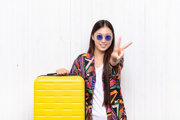 Mujer joven asiática sonriendo y luciendo feliz, despreocupada y positiva, gesticulando victoria o paz con una mano. concepto de vacaciones