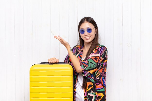 Mujer joven asiática sonriendo con orgullo y confianza, sintiéndose feliz y satisfecha y mostrando un concepto en el espacio de la copia. concepto de vacaciones