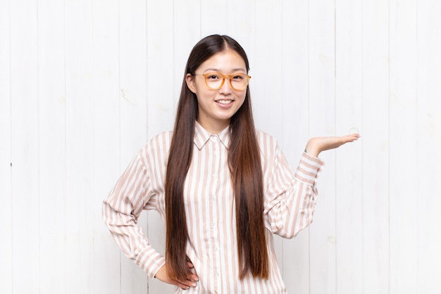 Mujer joven asiática sonriendo, sintiéndose confiada, exitosa y feliz, mostrando concepto o idea en el espacio de la copia en el lateral