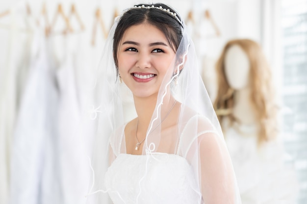 Mujer joven asiática sonriendo y tratando de vestido de novia en una tienda.