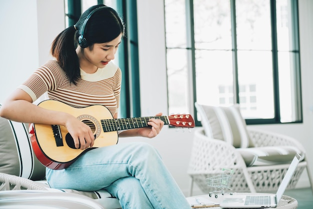 Mujer joven asiática tocando una guitarra para relajarse en la sala de estar