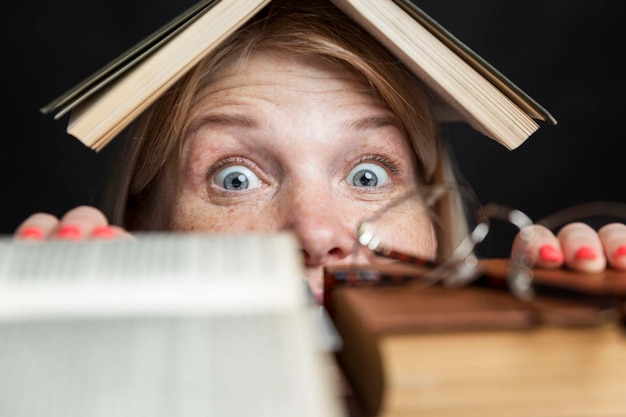 Una mujer joven se asoma horrorizada desde detrás de una pila de libros Gran volumen para lectura y educación Primer plano