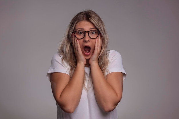 Mujer joven asombrada con gafas mirando a la cámara aislada sobre un fondo gris