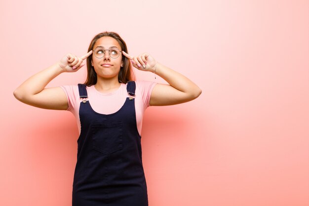 Mujer joven con aspecto concentrado y pensando mucho en una idea, imaginando una solución a un desafío o problema contra el fondo rosa