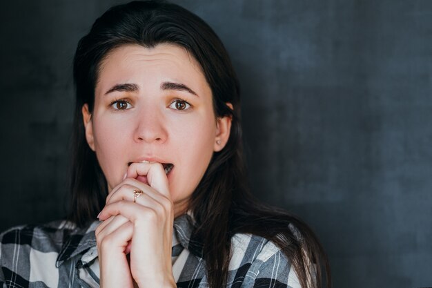 mujer joven asustada. morderse los dedos lágrimas en los ojos. fobia. expresión facial de emoción negativa.