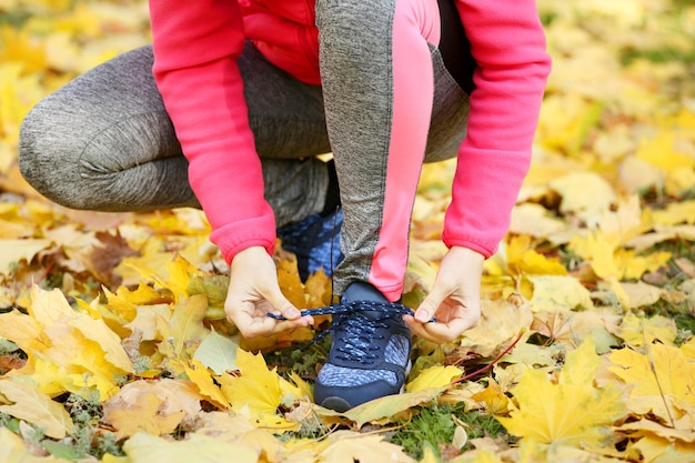 Foto mujer joven atando zapatos deportivos en el parque de otoño vista de cerca