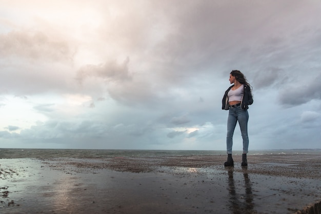 Mujer joven atendiendo cómo las olas golpean las rocas.