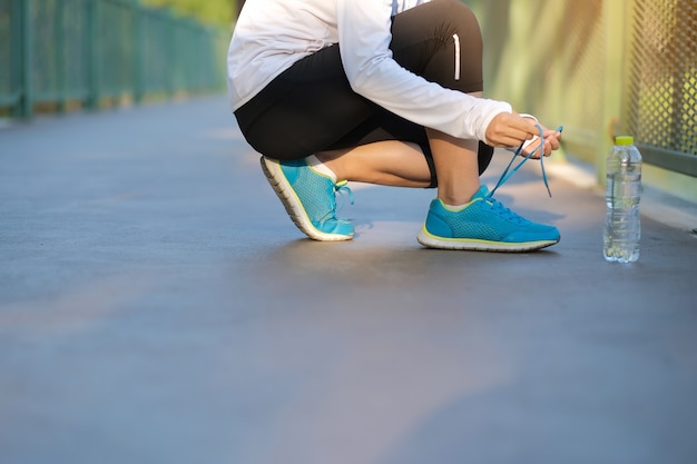 Mujer joven atleta atar zapatillas en el parque al aire libre