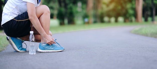 Mujer joven atleta atar zapatillas en el parque al aire libre