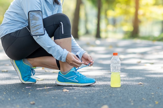 Mujer joven del atleta que ata las zapatillas deportivas en el parque al aire libre