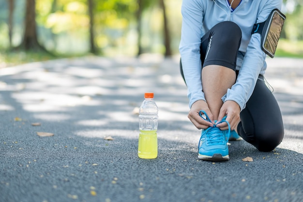 Mujer joven del atleta que ata las zapatillas deportivas en el parque al aire libre