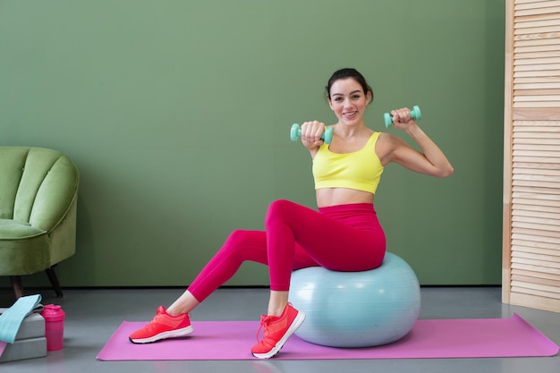 Mujer joven atlética en ropa deportiva haciendo ejercicios de estiramiento de fitness en casa en la sala de estar Concepto de deporte y cuidado corporal