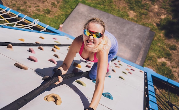 Mujer joven atlética trabajando y subiendo cuerdas en el campamento de entrenamiento de cuerdas