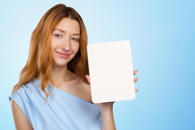 Mujer joven atractiva alegre que muestra la hoja de papel en blanco con el espacio de la copia