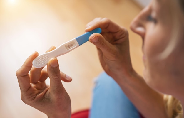 mujer joven y atractiva con anteojos sosteniendo una prueba de embarazo en casa mirando un resultado positivo en shock y estrés teniendo sorpresa en la imagen del concepto de maternidad no deseada de la niña