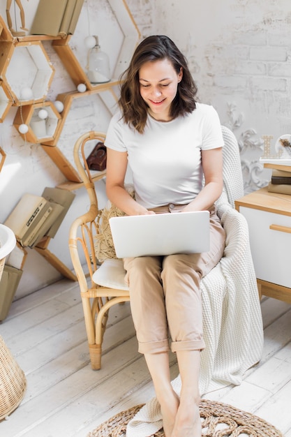 Una mujer joven y atractiva en un apartamento moderno y luminoso utiliza una computadora portátil para comunicarse o estudiar fotografías de alta calidad en línea