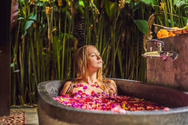 Mujer joven atractiva en el baño con pétalos de flores tropicales y aceites aromáticos Tratamientos de spa para el rejuvenecimiento de la piel Mujer seductora en el salón de spa Chica relajante en la bañera con pétalos de flores Lujo