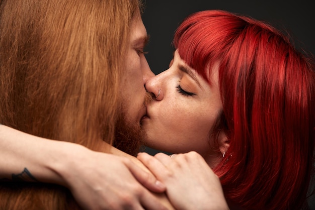 Una mujer joven y atractiva con cabello rubí brillante abraza y besa a un hombre con amantes semidesnudos de cabello largo