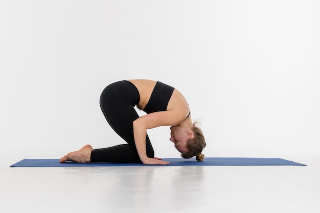 Mujer joven atractiva deportiva que hace práctica de la yoga en el fondo blanco.