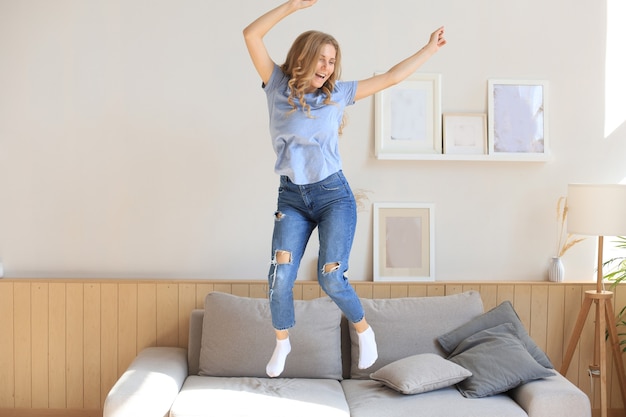 Foto la mujer joven atractiva se está divirtiendo en casa. la niña está saltando y bailando en el sofá.