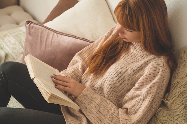 Mujer joven atractiva está leyendo un libro en casa