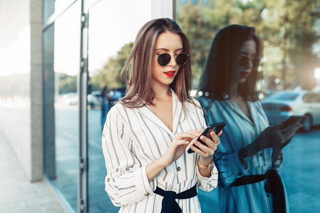 Foto mujer joven atractiva feliz en las gafas de sol que miran la pantalla del smartphone