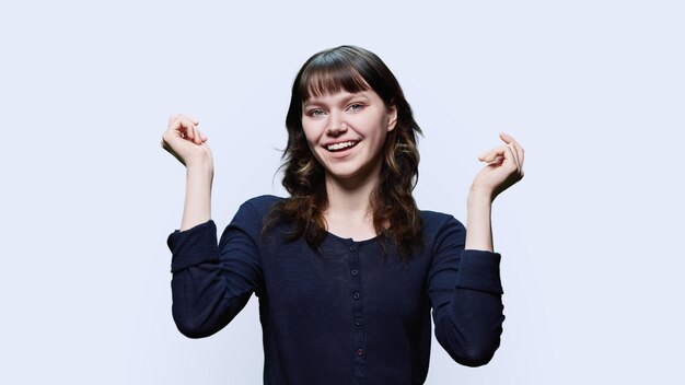 Mujer joven atractiva feliz con las manos en alto mirando a la cámara divirtiéndose en un fondo blanco de estudio Belleza moda juventud emociones positivas concepto