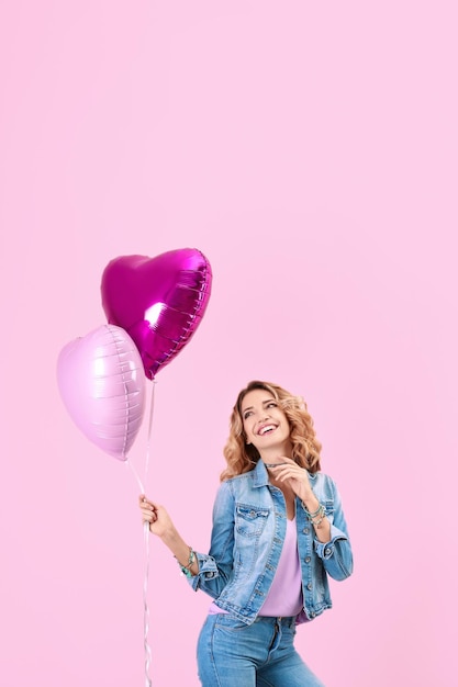 Mujer joven atractiva con globos de aire en forma de corazón sobre fondo de color